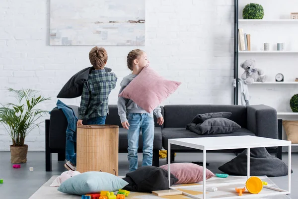 Cute brother and sister fighting with pillows and having fun at home — Stock Photo