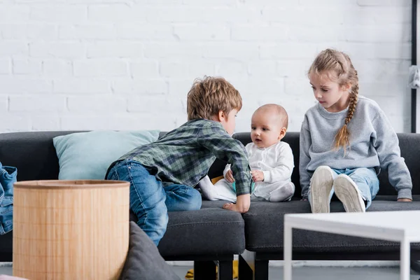 Mignon preteen frères et sœurs regardant adorable enfant en bas âge à la maison — Photo de stock