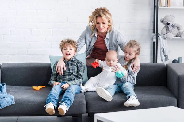 Mãe feliz olhando para três crianças adoráveis sentados no sofá — Fotografia de Stock