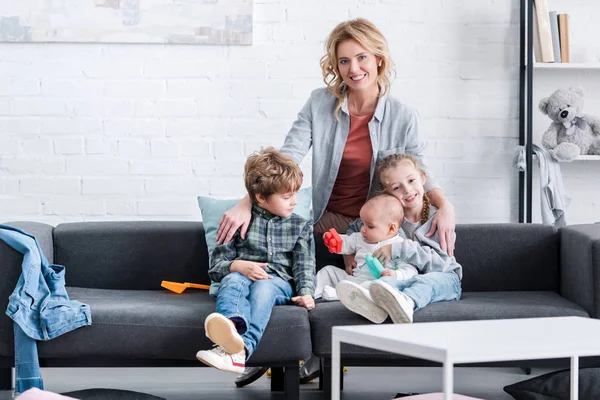 Feliz madre sonriendo a la cámara mientras pasa tiempo con tres adorables niños pequeños en casa - foto de stock