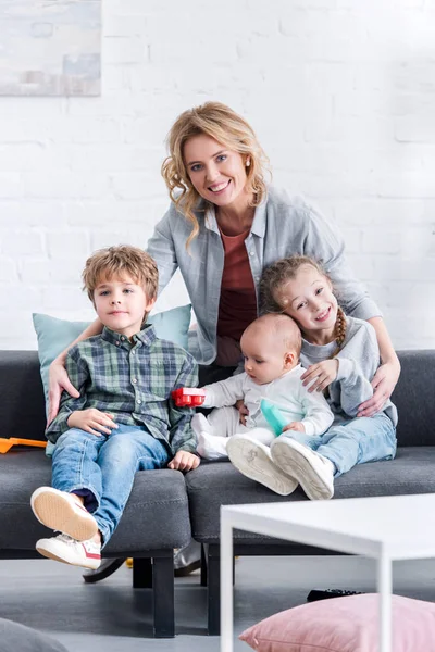 Mère heureuse avec trois adorables petits enfants sur le canapé à la maison — Photo de stock
