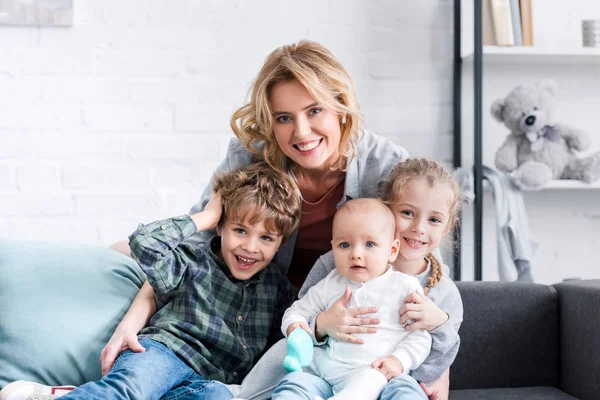 Beautiful happy mother with three adorable children smiling at camera — Stock Photo