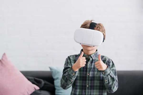 Menino usando fone de ouvido realidade virtual e mostrando os polegares para cima em casa — Fotografia de Stock