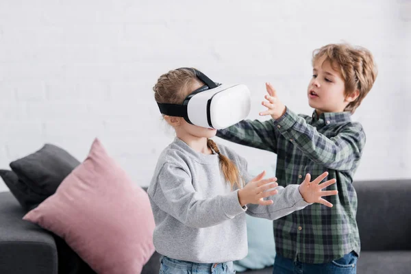 Irmãos adoráveis brincando com fone de ouvido realidade virtual em casa — Fotografia de Stock