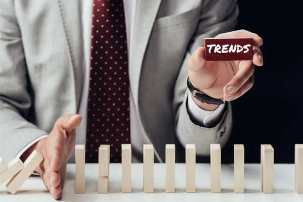 Partial view of businessman holding brick with 'trends' word and preventing wooden blocks from falling — Stock Photo