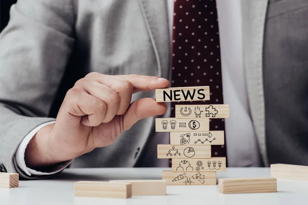 Cropped view of man holding brick with word 'news' over wooden blocks with icons — Stock Photo