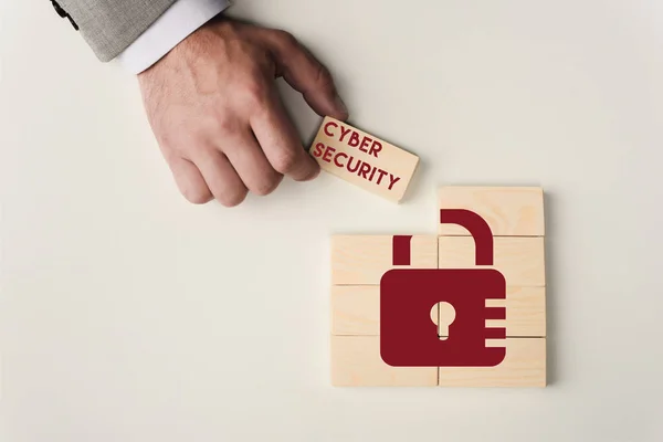 Partial view of man holding brick with 'cyber security' lettering over wooden blocks with lock icon isolated on white — Stock Photo