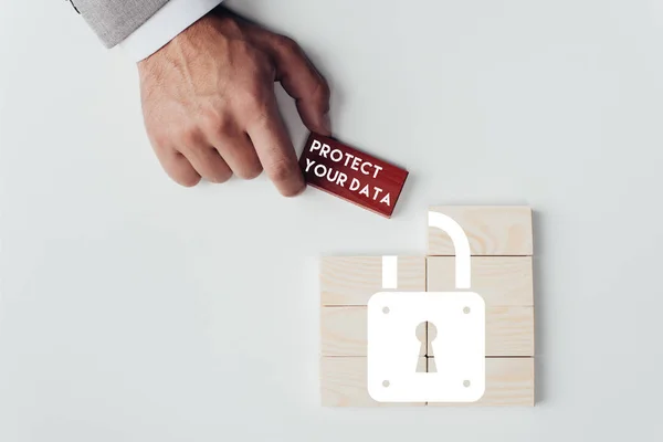 Vista parcial del hombre sosteniendo ladrillo con letras de 'proteger sus datos' sobre bloques de madera con icono de bloqueo aislado en blanco - foto de stock