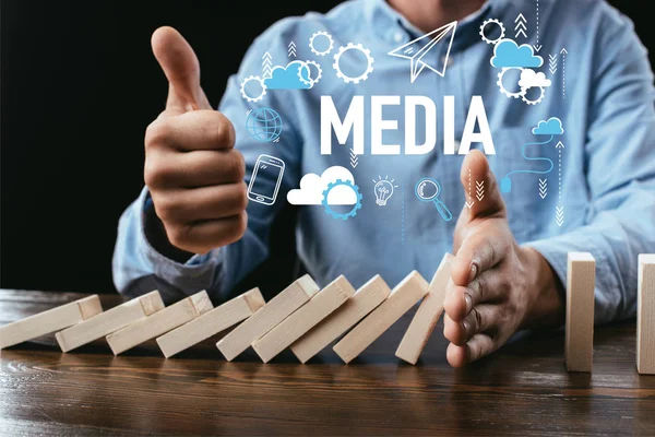 Partial view of man showing thumb up sign while preventing wooden blocks from falling with word and icons on foreground — Stock Photo