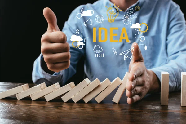 Partial view of man showing thumb up sign while preventing wooden blocks from falling with word and icons on foreground — Stock Photo