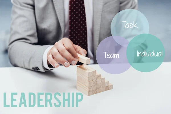 Cropped view of man building career ladder with wooden blocks, icons and 'leadership' lettering on foreground — Stock Photo