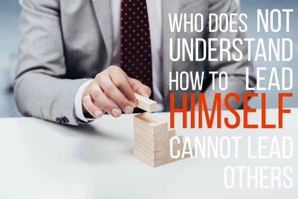 Cropped view of man building career ladder with wooden blocks, 'who does not understand how to lead himself cannot lead others' lettering on foreground — Stock Photo