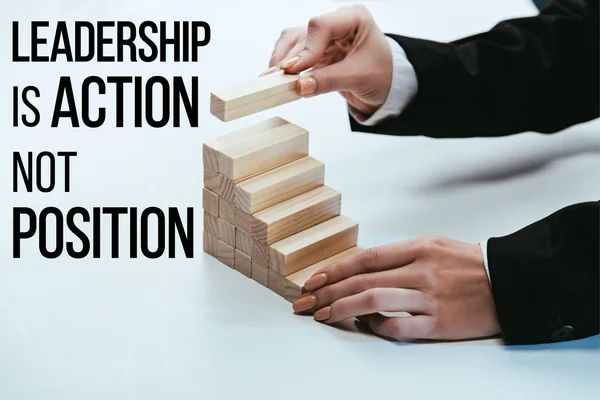 Cropped view of woman building career ladder with wooden blocks, 'leadership is action not position' lettering on foreground — Stock Photo