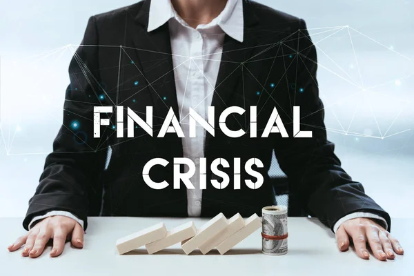 Cropped view of businesswoman with wooden blocks and money roll on table and 'financial crisis' lettering on foreground — Stock Photo