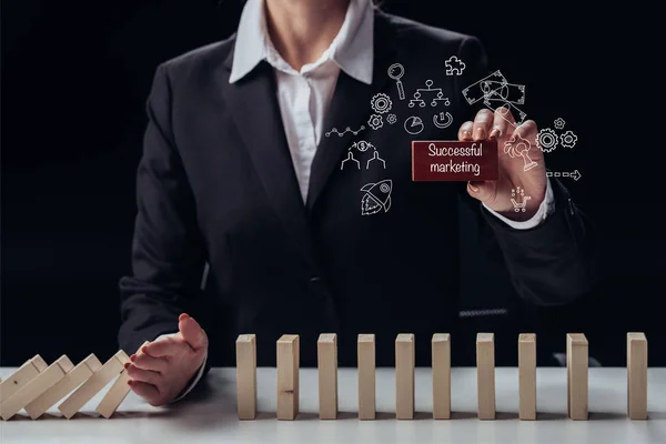 Cropped view of businesswoman holding red brick with words 'successful marketing' while preventing wooden blocks from falling, icons on foreground — Stock Photo