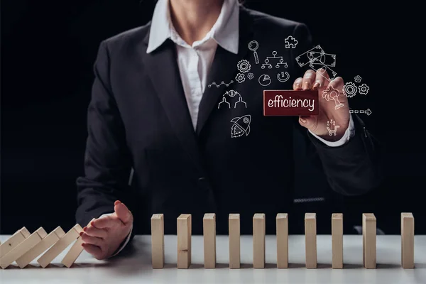 Cropped view of businesswoman holding red brick with 'efficiency' word while preventing wooden blocks from falling, icons on foreground — Stock Photo