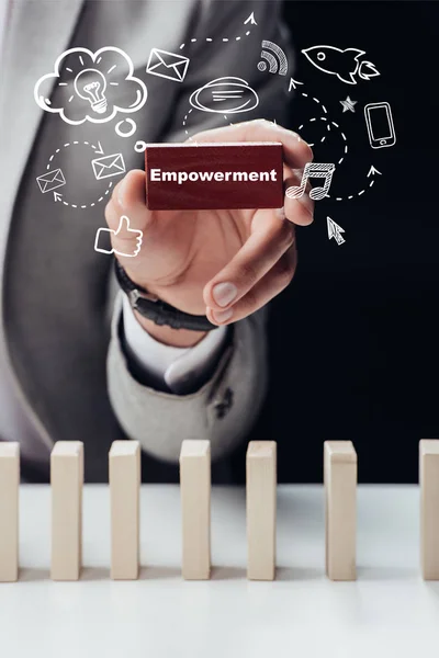 Partial view of man holding red brick with word 'empowerment' isolated on black, icons on foreground — Stock Photo