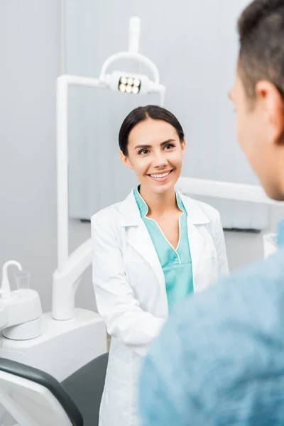 Sorridente dentista feminina olhando para paciente afro-americano em consultório odontológico — Fotografia de Stock