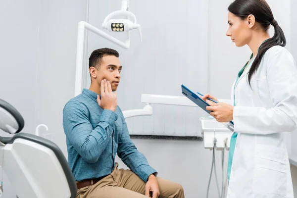 Dentista femminile in piedi vicino al paziente afro-americano con mal di denti — Foto stock