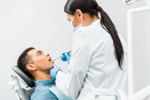 Dentista femenina en guantes de látex examinando paciente afroamericano - foto de stock
