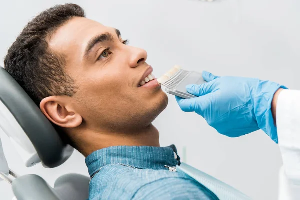 Handsome african american man smiling near teeth color palette before whitening procedure — Stock Photo