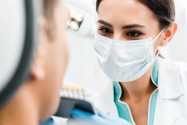 Selective focus of female dentist holding teeth color palette near african american patient — Stock Photo