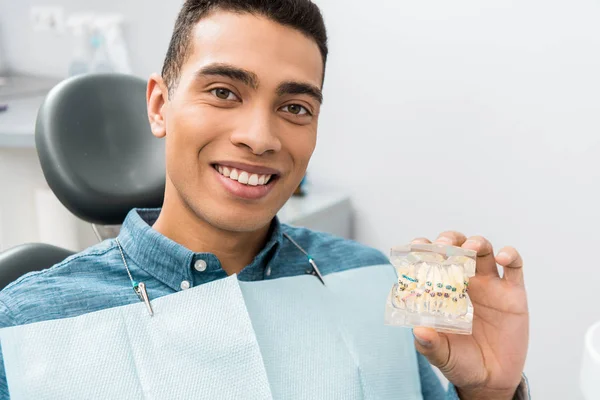 Bonito afro-americano homem segurando modelo de mandíbula dental com aparelho — Fotografia de Stock