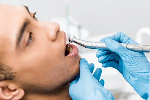 Primer plano del dentista femenino perforando los dientes del paciente afroamericano - foto de stock