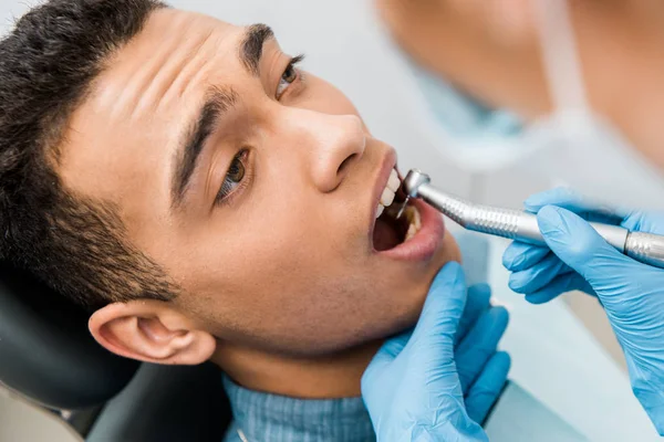 Primer plano de las manos del dentista perforando los dientes del paciente afroamericano - foto de stock