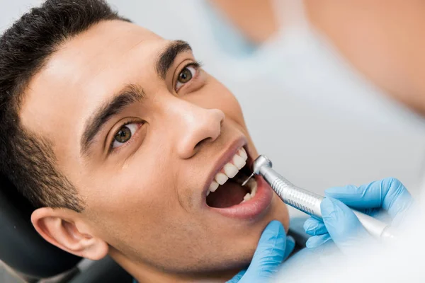 Крупным планом женщины-стоматолога сверлит зубы красивого африканского пациента из Америки — стоковое фото