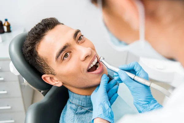 Female dentist drilling teeth of handsome african american patient — Stock Photo