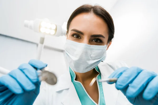 Enfoque selectivo del dentista femenino en la máscara que sostiene los instumentos en las manos - foto de stock