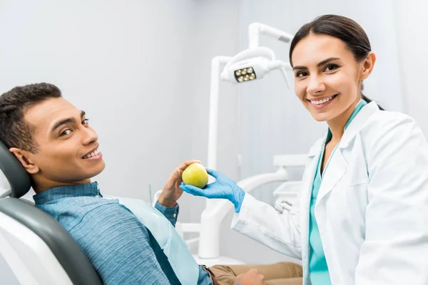 Dentista sorrindo dando maçã para paciente afro-americano — Fotografia de Stock