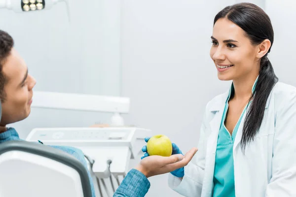 Dentista atraente dando maçã ao paciente — Fotografia de Stock