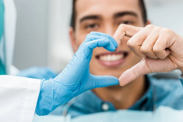 Messa a fuoco selettiva di dentista e mani di paziente afro-americano rendendo la forma del cuore — Foto stock