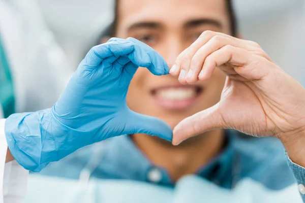 Enfoque selectivo de las manos en forma de corazón de dentista y paciente afroamericano - foto de stock