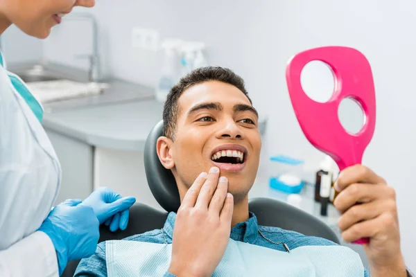 Alegre afroamericano hombre tocando la cara y mirando el espejo - foto de stock