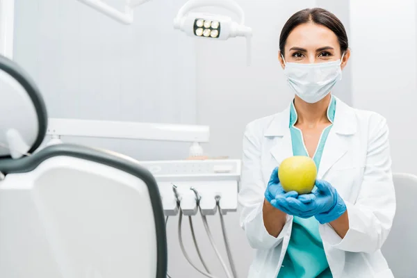Dentista donna in mantello bianco e maschera con mela in mano — Foto stock