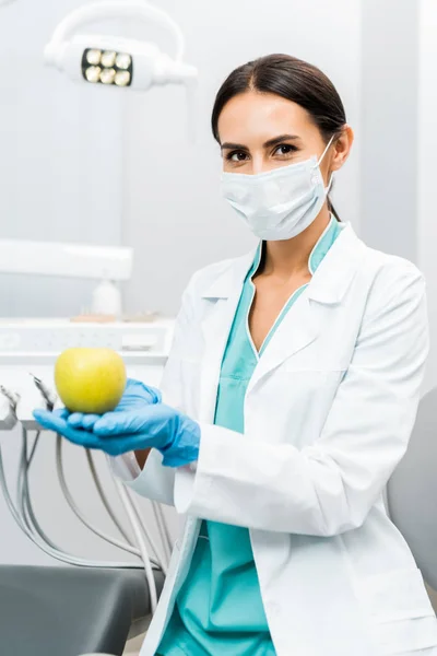 Estomatóloga femenina con abrigo blanco y máscara sosteniendo manzana - foto de stock