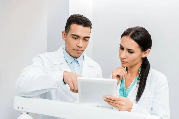 Médicos multiétnicos graves mirando tableta digital - foto de stock
