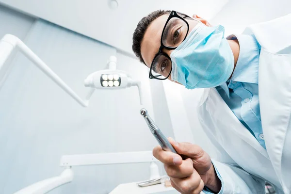 Dentista afroamericano en máscara y gafas con taladro en la mano - foto de stock