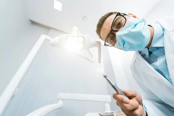 Dentista afroamericano in cappotto bianco e maschera con trapano in mano — Foto stock