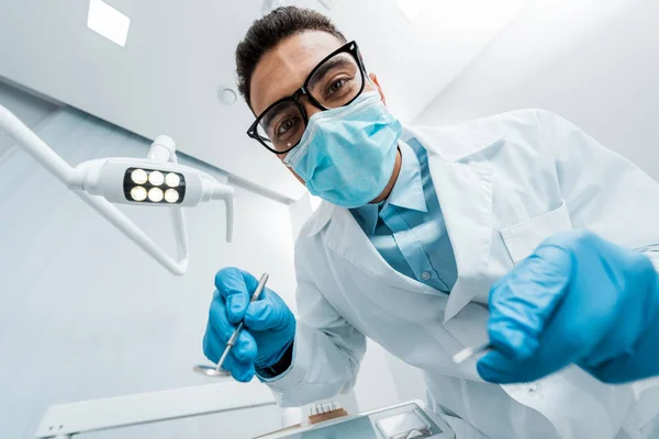 African american stomatologist in glasses and mask with dental instruments in hands — Stock Photo