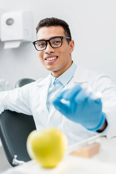 Foco seletivo do dentista americano africano masculino usando luva de látex perto de maçã doce — Fotografia de Stock