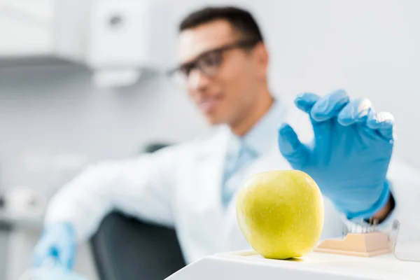 Selective focus of hand of male african american dentist wearing latex glove near sweet apple — Stock Photo