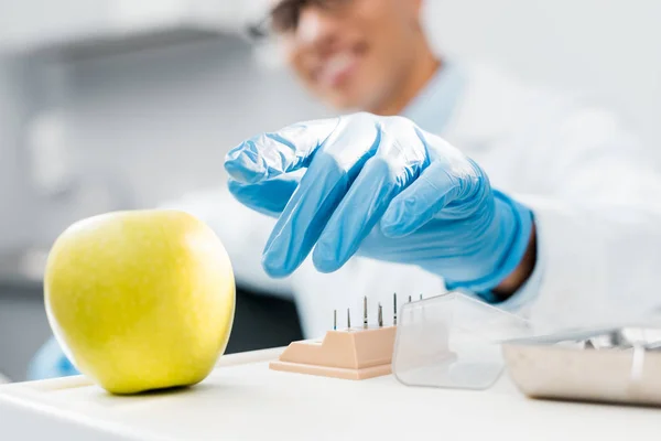 Selective focus of hand of male african american dentist wearing latex glove near tasty apple — Stock Photo