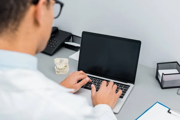 Selective focus of male doctor typing on laptop with blank screen — Stock Photo