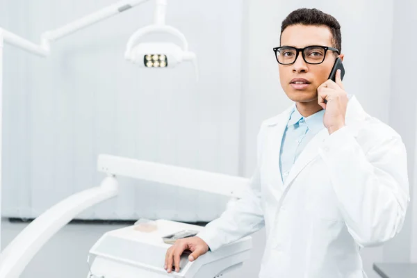 Sério dentista afro-americano em óculos falando no smartphone — Fotografia de Stock