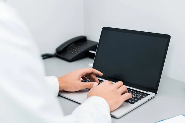 Enfoque selectivo de manos masculinas del médico afroamericano escribiendo en el ordenador portátil con pantalla en blanco - foto de stock