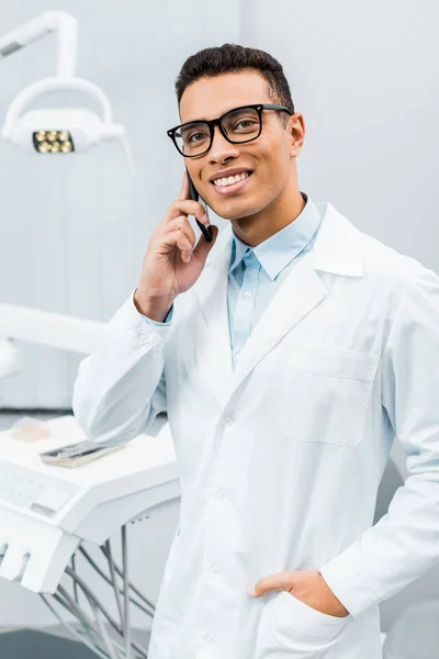 Handsome african american doctor in glasses talking on smartphone with hand in pocket — Stock Photo